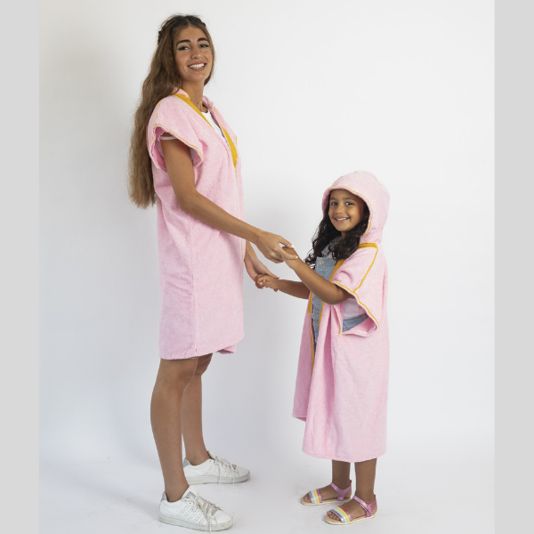 A mom is wearing Beach Bisht kids hoodie bathrobe large size, daughter is wearing kids hoodie bathrobe small size both wearing pink color  from beach bisht terry towel beach cover up kimono collections